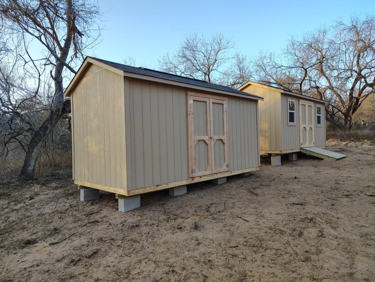 Two wooden sheds on sandy ground